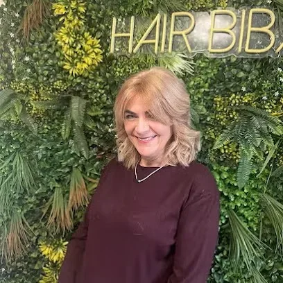 Client with a blonde curly bob in front of the HairBiba neon sign